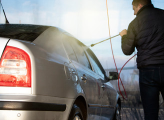 Car wash. A man washes a car under the pressure of water and rubs the glass. Car care concept