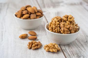 Almond seeds and walnuts in white bowls on wood table