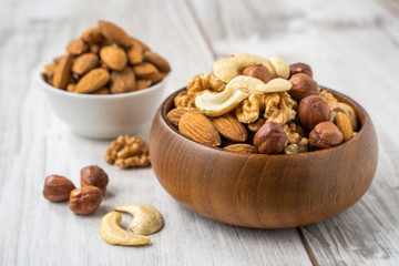 Different nuts in white and wooden bowls on wood table