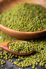 Mung bean, green moong in a wooden plate and spoon, on black metallic vintage background. Copy space. Black background. Scattered mung bean. Eco wooden spoon and plate. top view.