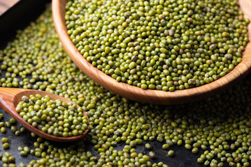 Mung bean, green moong in a wooden plate and spoon, on black metallic vintage background. Copy space. Black background. Scattered mung bean. Eco wooden spoon and plate. top view.