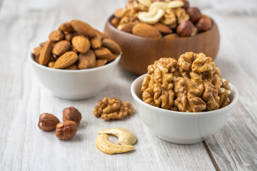 Different nuts in white and wooden bowls on wood table
