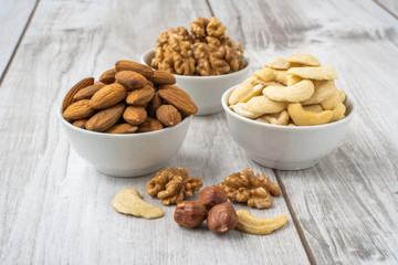 Different nuts in white bowls on wood table