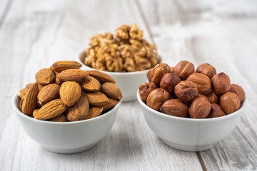 Different nuts in white bowls on wood table