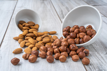 Scattered hazlenuts and almond seeds with white bowls on wood table