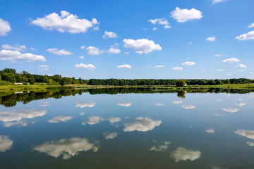 Beautiful landscape, reflection in clear water. Lake against the blue sky with white fluffy clouds.