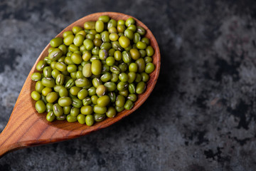 Mung bean, green moong in a wooden spoon, on black metallic vintage background. Copy space. Black background. Scattered mung bean. Eco spoon. 