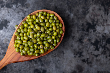 Mung bean, green moong in a wooden spoon, on black metallic vintage background. Copy space. Black background. Scattered mung bean. Eco spoon. 