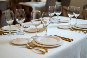 Chic and elegant, gold-plated cutlery and white plates, table setting with empty plates. The hall is lit by natural light.