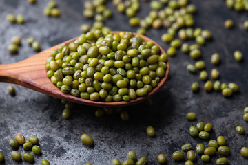 Mung bean, green moong in a wooden spoon, on black metallic vintage background. Copy space. Black background. Scattered mung bean. Eco spoon. 