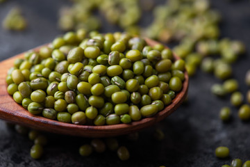 Mung bean, green moong in a wooden spoon, on black metallic vintage background. Copy space. Black background. Scattered mung bean. Eco spoon. 