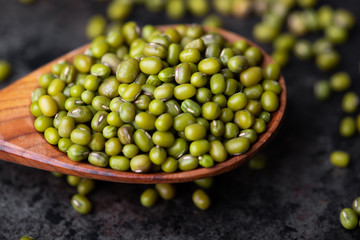 Mung bean, green moong in a wooden spoon, on black metallic vintage background. Copy space. Black background. Scattered mung bean. Eco spoon. 