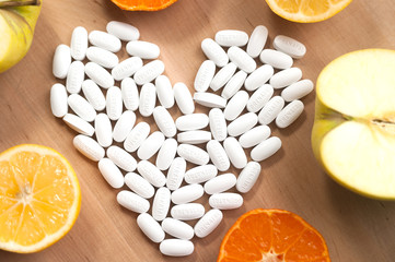 pills laid out in the shape of a heart on a background of fruits