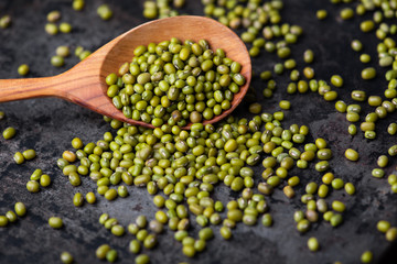 Mung bean, green moong in a wooden spoon, on black metallic vintage background. Copy space. Black background. Scattered mung bean. Eco spoon. 