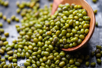 Mung bean, green moong in a wooden spoon, on black metallic vintage background. Copy space. Black background. Scattered mung bean. Eco spoon. 