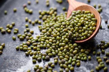 Mung bean, green moong in a wooden spoon, on black metallic vintage background. Copy space. Black background. Scattered mung bean. Eco spoon. 