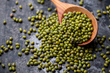 Mung bean, green moong in a wooden spoon, on black metallic vintage background. Copy space. Black background. Scattered mung bean. Eco spoon. 