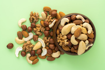 Different nuts in wooden bowl on green background