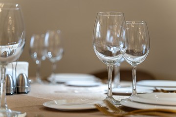 Chic and elegant, gold-plated cutlery and white plates, table setting with empty plates. Glasses in the light from the window-2.