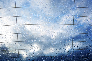Krople deszczu na tylnej szybie samochodu z chmurami w tle.