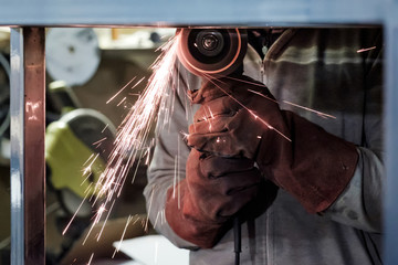 Man in protective gloves cutting metal using angle grinder making sparks