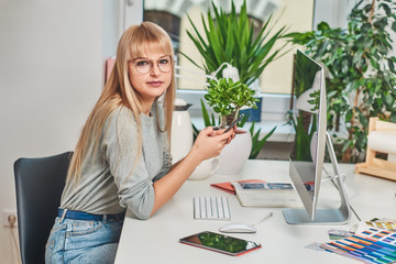Young pretty woman in glasses is holding a mobile phone while sitting in the office.