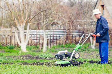 Fototapeta na wymiar A man plows the land with a cultivator in a spring garden