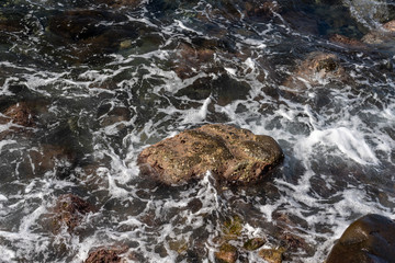 Water flows over rocks. Restless sea with foamed waves and rocks. 