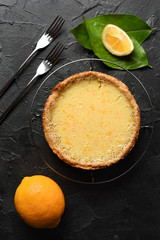 Homemade rustic dessert. Tasty open lemon pie with wholegrain crust served with raw lemons and forks on black background copy space