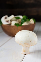 still life, champignon mushrooms with herbs in a wooden bowl on a white table