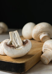 still life, champignon mushrooms on a cutting wooden board with black background