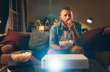young man watching projector tv at home in   evening alone.