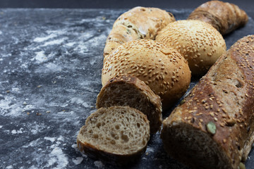 On a black background baguette with sesame seeds and pumpkin seeds and round buns and croissants
