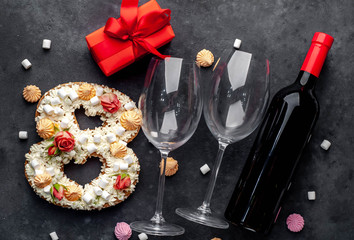 a cake in the shape of 8 is decorated with flowers, cream cheese, marshmallows, Bizet with a bottle of wine and glasses on a stone background. holiday concept dinner for two on March 8.