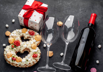 Obraz na płótnie Canvas a cake in the shape of 8 is decorated with flowers, cream cheese, marshmallows, Bizet with a bottle of wine and glasses on a stone background. holiday concept dinner for two on March 8.