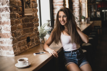 Woman using phone and drinking coffee in a cafe.