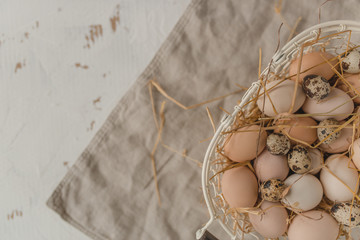 Fresh chicken and quail eggs with straw in a basket on a rustic style linen background. Easter concept. Healthy lifestyle concept.