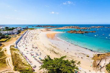 Aerial view over the white sandy beach of Greve Blanche in Tregastel, northern Brittany, France, on a sunny summer day with dozens of people sunbathing and enjoying the turquoise sea. - Powered by Adobe