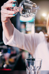 The girl bartender pours burning sambuca in a glass