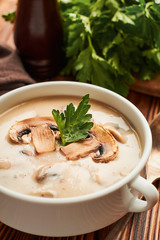 A bowl of mushroom soup with parsley on wooden table vertical shot