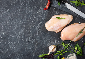 Fresh raw chicken fillet, spices and herbs on black stone background, top view
