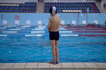 young boy stand at the side of the swimming pool looking sad.