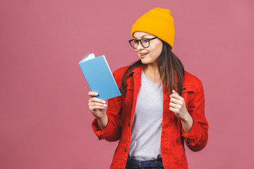 Beautiful young woman wearing casual standing isolated over pink background, reading a book.