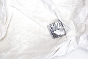 A Open condom package on white sheets of a bed, contraceptives couple relation intercourse