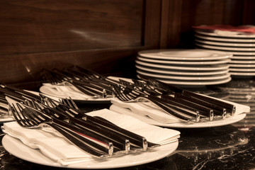 Plates with knifes and forks on the wooden credence