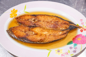 Delicious Natural Fresh Deep Fried King Mackerel Fish with Fish Sauce on white plate with table background. Thailand Food, Asian Cuisine, Thai Casual Food, Seafood and Street Food dish menu concept.
