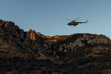 Fototapeta na wymiar Helicopter flight over mountainous valley. Rescue helicopter fly in a remote location in dusk. Landscape with a rocky canyon