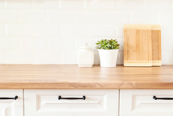 Fototapeta na wymiar Bright And Clean Kitchen With White Cabinets, Close Up. Cutting Boards, Green Succulent Pot On A Wooden Worktop. Kitchenware In Modern Kitchen Interior. White Tiles Background