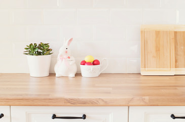 Easter Eggs, Rabbit, Cutting Boards, Succulent On The Kitchen Counter. Bright And Clean Rustic Kitchen With White Cabinets, Close Up. Kitchenware In Modern Kitchen Interior. White Tiles Background