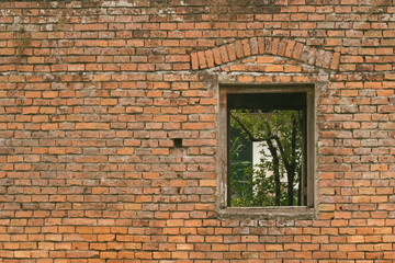 Old brick wall with a window and trees behind